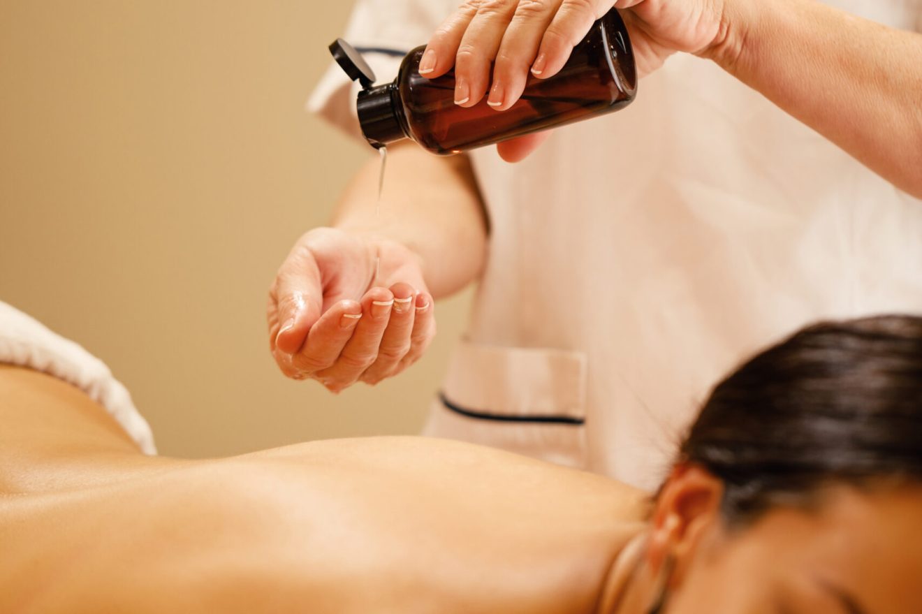 Unrecognizable therapist pouring oil in her hands before massage treatment at the wellness center,
